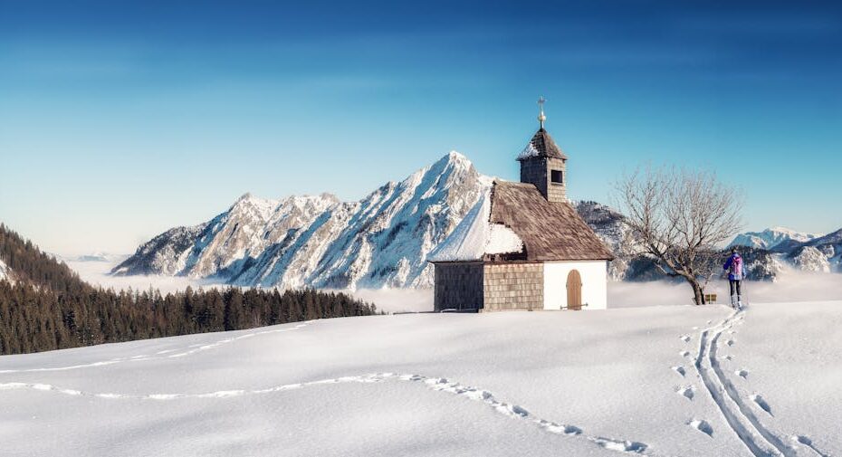 A serene winter scene with a chapel, snowy mountains, and skier in Strobl, Austria.