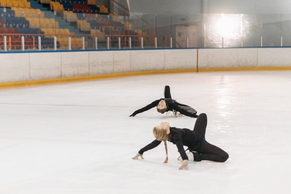Two young figure skaters practicing their moves on an indoor ice rink.